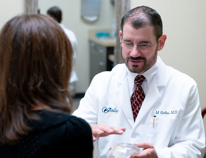 Doctor Gallas consulting a client while holding a breast implant.