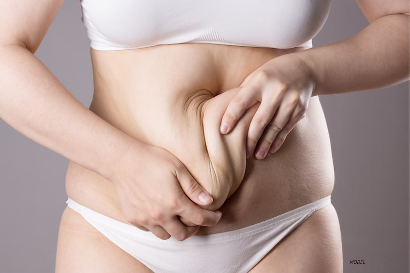 Woman in white underwear pinching excess skin on her midsection