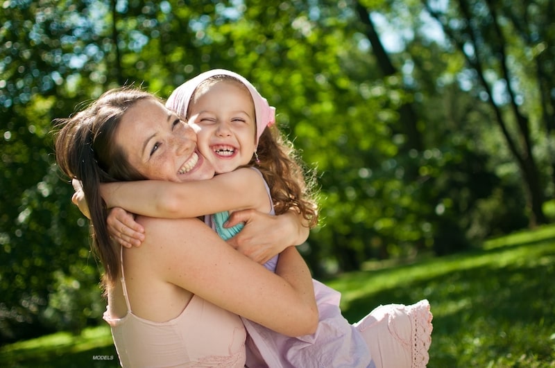 Mother hugging her daughter outdoors.