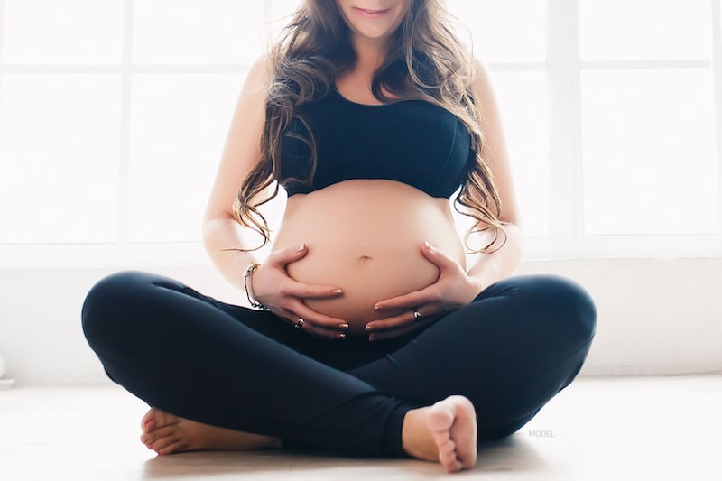 Seated pregnant woman with her hands on her belly.