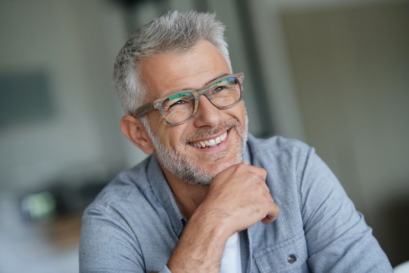 Handsome middle-aged man, wearing glasses and smiling as he puts his hand to his chin.