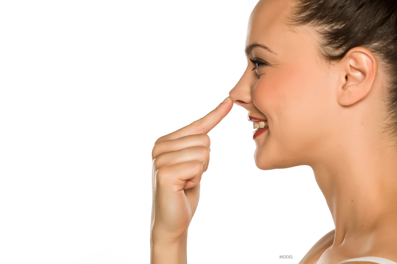 young happy woman touches her nose with her finger on a white background